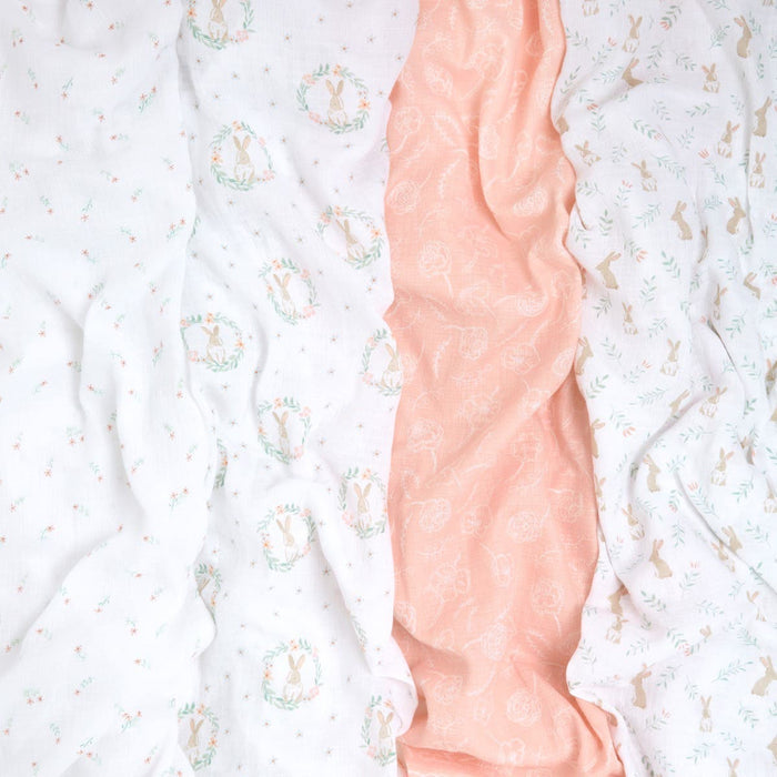 Aden + anais essentials cotton muslin swaddles 4 pack includes crinkled pastel fabrics: white with small florals, soft pink with subtle patterns, white with rabbits in circular designs, and white featuring delicate green and brown rabbit motifs.