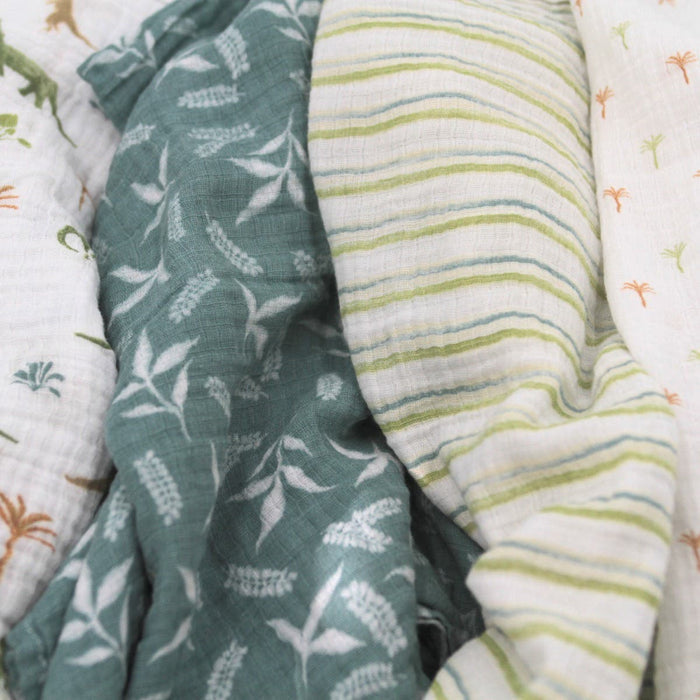A close-up of aden + anais essentials cotton muslin swaddles shows patterns like green foliage on dark, green/white stripes, and tree motifs on white. Made from breathable cotton, these textured and layered swaddles ensure comfort.