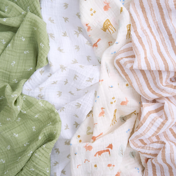 The aden + anais essentials cotton muslin swaddle blanket 4 pack offers versatile, breathable blankets in soft patterns and colors: green with arrows, white with small motifs, cream with animal prints, and beige stripes, all elegantly overlapped.