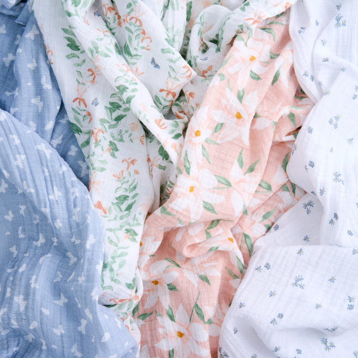 Explore aden + anais essentials cotton muslin swaddle blanket 4 pack featuring crumpled cotton muslin in patterns like light blue with white motifs, white with tiny blue designs, green leaves on white, and large peach flowers. Perfect for swaddles or versatile use.