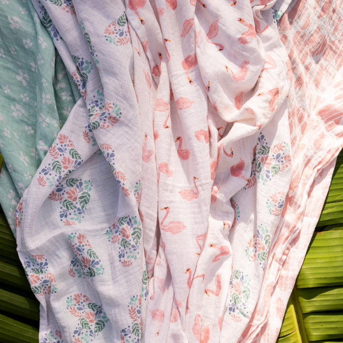 The aden + anais essentials cotton muslin swaddle blanket 4 pack features a soft, versatile fabric with patterns such as flamingos, floral designs, and leaves in pastel shades of pink, blue, and green.
