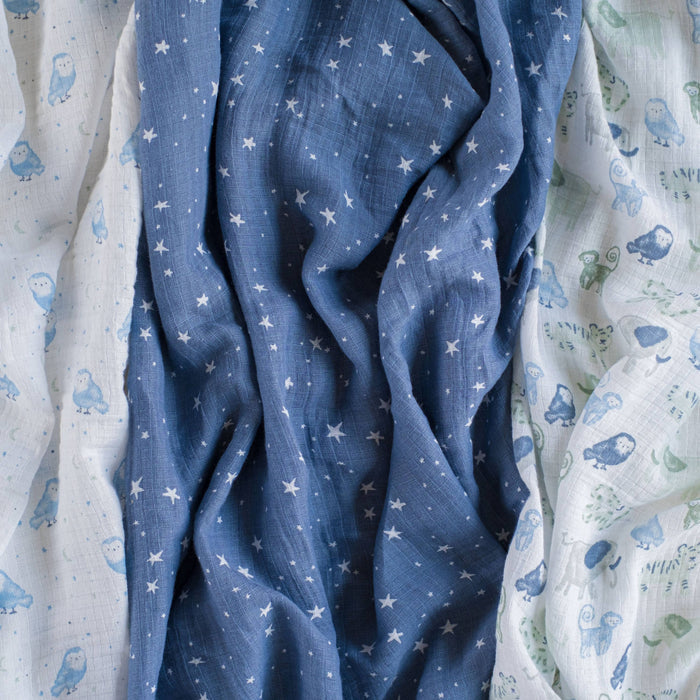 The aden + anais essentials cotton muslin swaddle blanket 4 pack features crumpled fabrics: white with blue owls, blue with white stars, and white with assorted blue and green birds. These soft, wrinkled textures indicate they are versatile, breathable, and lightweight.
