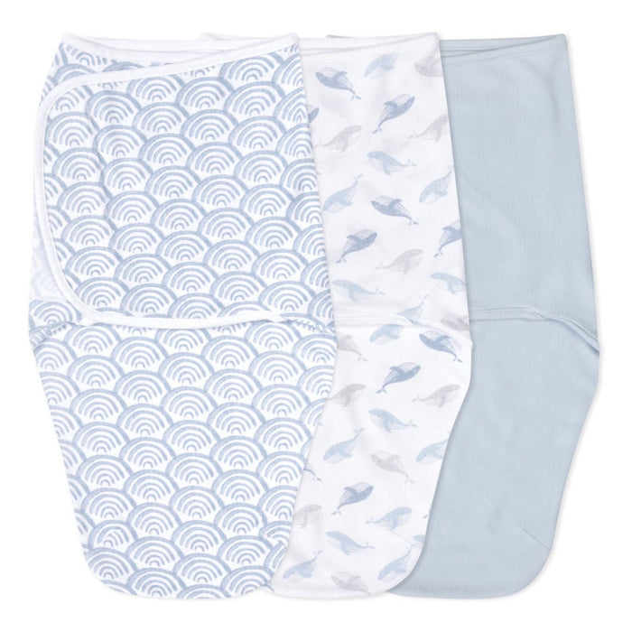 The essentials easy swaddle wrap 3 pack by aden + anais includes wraps with blue waves, whale patterns, and a light blue design. Each swaddle has adjustable fasteners to prevent the startle reflex and is neatly laid flat in a row.