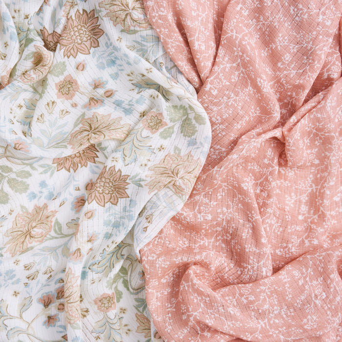 A close-up of aden + anais essentials silky soft swaddle blanket 2 pack shows a bamboo-infused floral pattern on white, and a pink geometric design. Both fabrics are softly draped, highlighting their gentle folds and textures, perfect for babys sensitive skin.