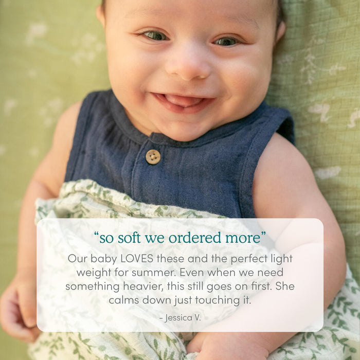 A smiling baby in a sleeveless navy top is wrapped in an aden + anais Bamboo Baby Bundle, featuring a green and white print. Overlaid text highlights Jessica V.s praise for the blanket’s exceptional softness and comfort.