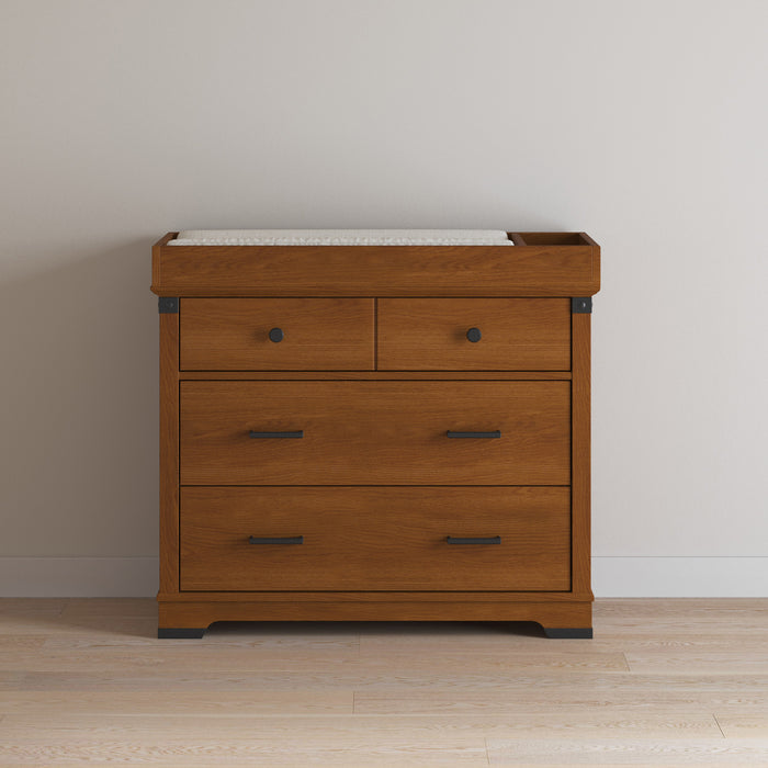 The Child Craft F01792 Universal Dressing Kit in Coach Cherry sits atop a wooden dresser with two small upper drawers and two larger lower drawers, all with black handles, set against a light wall and wooden floor.