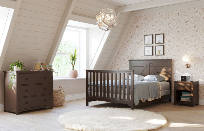 A cozy attic bedroom with sloped ceilings, a large window, and natural light. Features the Child Craft F06401 Full-Size Bed Rails in Brushed Truffle, matching nightstand and dresser, plants, accent wall, and white rug on light wood floors.