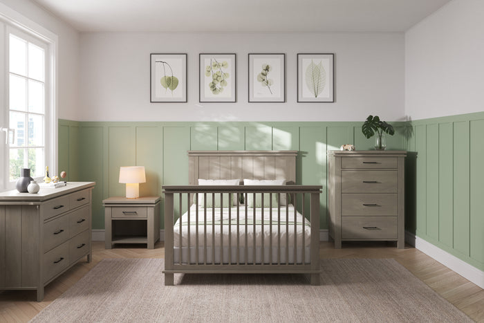 A bright bedroom with green wainscoting, a Child Craft bed featuring F06424 Full-Size Bed Rails in Midnight Grey, matching dresser, nightstand with lamp, and chest of drawers. Leaf artwork hangs above as sunlight fills the space.