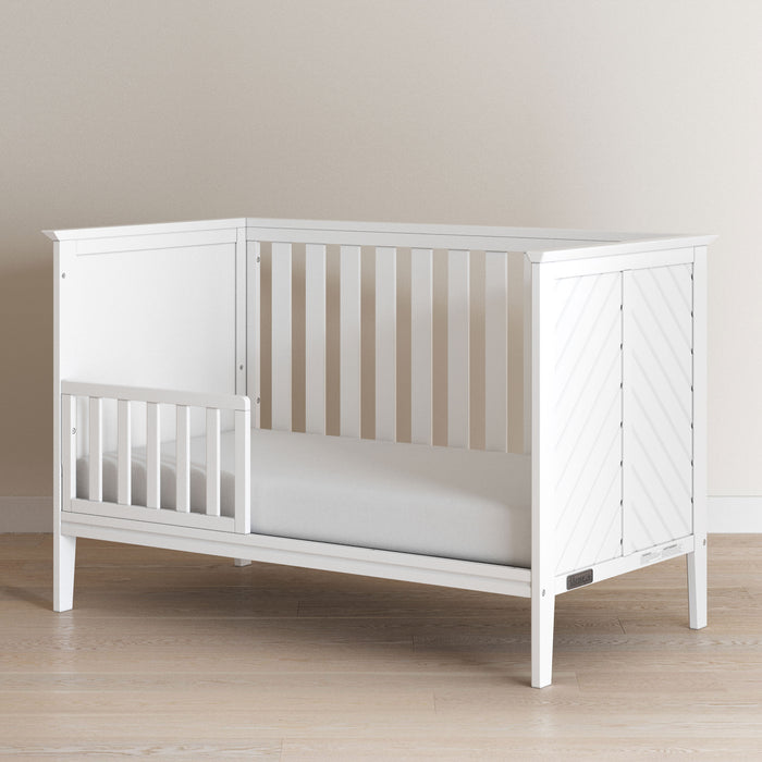 The Child Craft F09501 Toddler Guard Rail in matte white, featuring sturdy wood construction and slatted sides with a partial guard rail, sits on a light wood floor against a neutral wall.