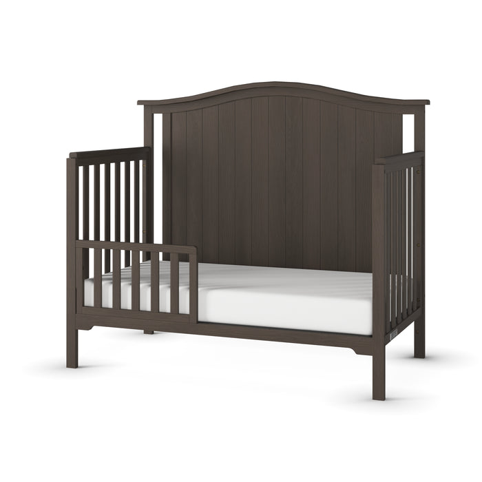 The Child Craft F09501 Toddler Guard Rail in Dapper Gray features sturdy wood, a high curved headboard, slatted rails, and a partially open front for easy access. Includes a white mattress; perfect for safe and stylish toddler sleep.