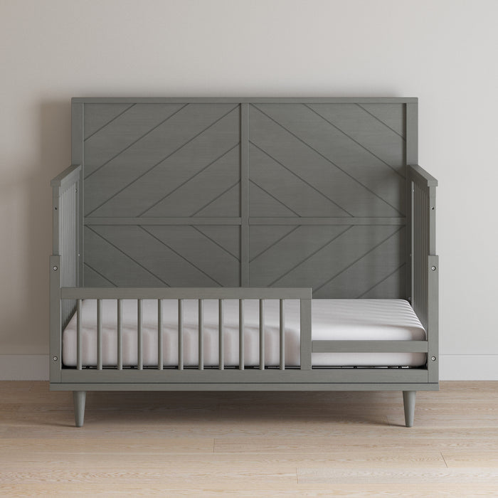 The Child Craft F09502 Toddler Guard Rail in Lunar Gray features a geometric design and partial side rails for safety, paired with a white mattress on a light wood floor against a plain light-colored wall.