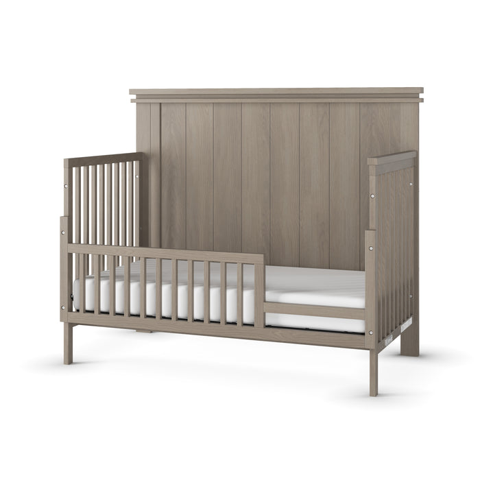 The Child Craft F09503 Toddler Guard Rail in Crescent Grey features a high paneled headboard, open sides with vertical slats, and a guard rail. Modern design fits perfectly after converting from a Child Craft crib; includes white mattress.