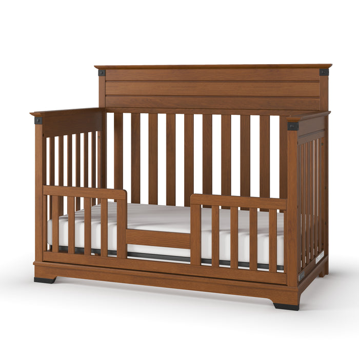 The Child Craft F09514 Toddler Guard Rail in Coach Cherry features sturdy wood construction with a brown finish, vertical slats on all sides, a partially open front with a low guard rail, flat headboard, and includes a white mattress.