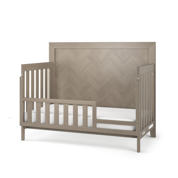 The Child Craft F09554 Toddler Guard Rail in Crescent Gray safely converts your Child Craft crib to a toddler bed, featuring a stylish design with open slats shown here in a modern gray finish and paired with a white mattress.