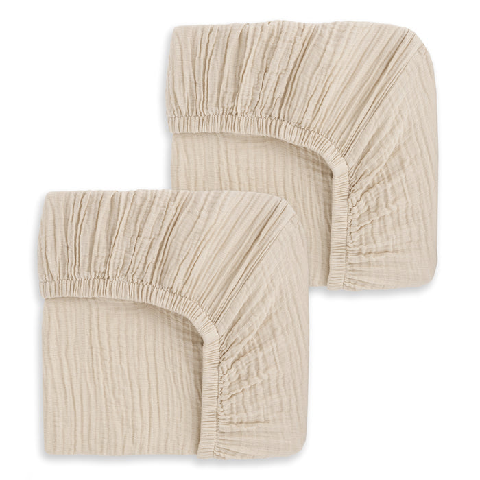 Two HALO Fitted Crib Sheets, 100% Organic Cotton Muslin, in beige, folded and stacked with gathered elastic edges shown against a white background. Set of 2 pack.