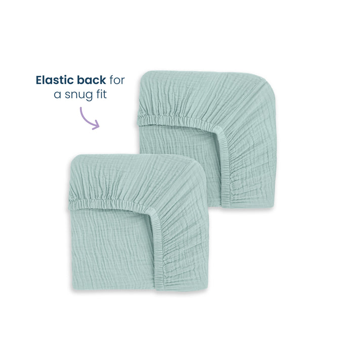 Two folded HALO Fitted Crib Sheets (100% Organic Cotton Muslin, 2 Pack) in light blue are shown on a white background, with text and an arrow indicating the elastic back provides a snug fit.