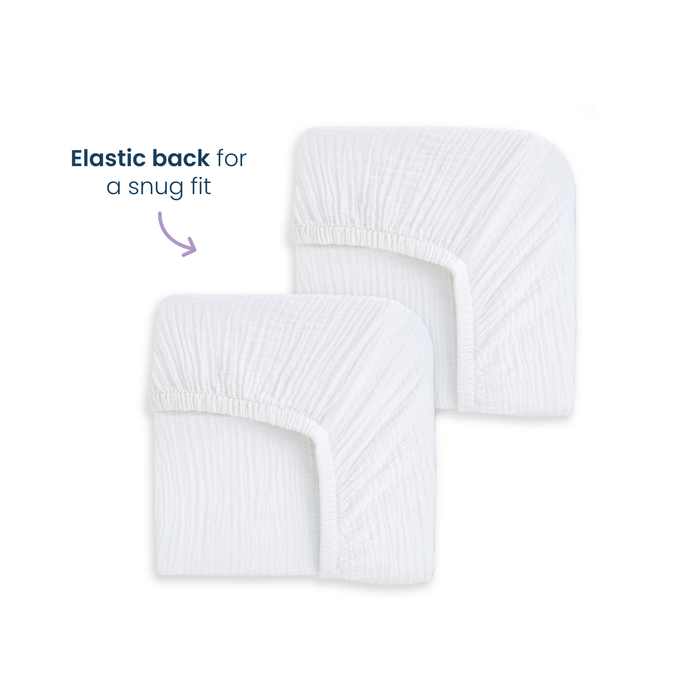 Two HALO Fitted Crib Sheets 100% Organic Cotton Muslin (2 Pack) are shown on a plain white background. An arrow points to the elastic, captioned: Elastic back for a snug fit, highlighting their secure and breathable design.