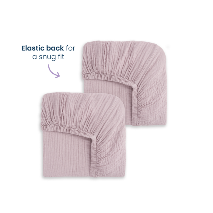 HALO Fitted Crib Sheets 100% Organic Cotton Muslin 2 Pack in light purple are shown folded to display their elastic backs for a snug fit. These breathable, textured sheets add cozy comfort to any crib.