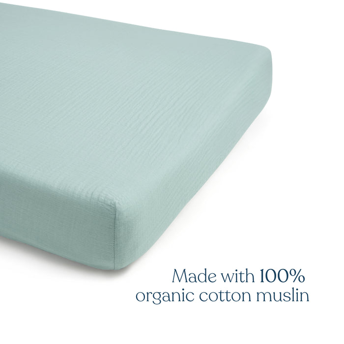 A light blue HALO Fitted Crib Sheet made from 100% organic cotton muslin covers a mattress corner. The text reads: HALO Fitted Crib Sheets 2 Pack—breathable, soft, and made with organic cotton muslin.