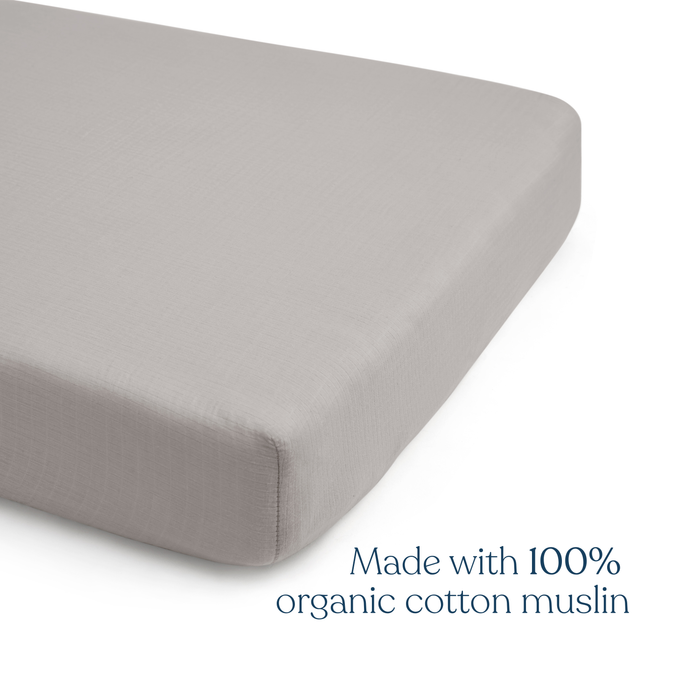 A close-up of a HALO Fitted Crib Sheet 100% Organic Cotton Muslin from the 2 Pack set, shown on a mattress corner, with “Made with 100% organic cotton muslin” in blue in the lower right corner.