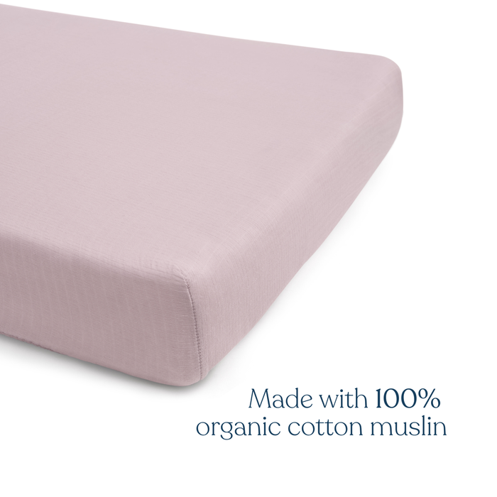 A light mauve HALO Fitted Crib Sheet covers a mattress corner. Text: HALO Fitted Crib Sheets 100% Organic Cotton Muslin 2 Pack—soft, breathable comfort for your baby’s crib.