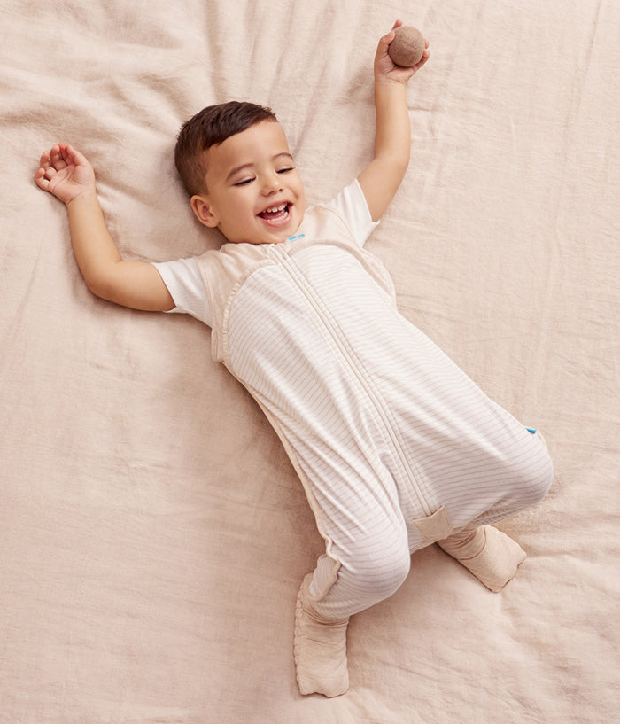 Child wearing a white baby grow lying on a soft beige surface