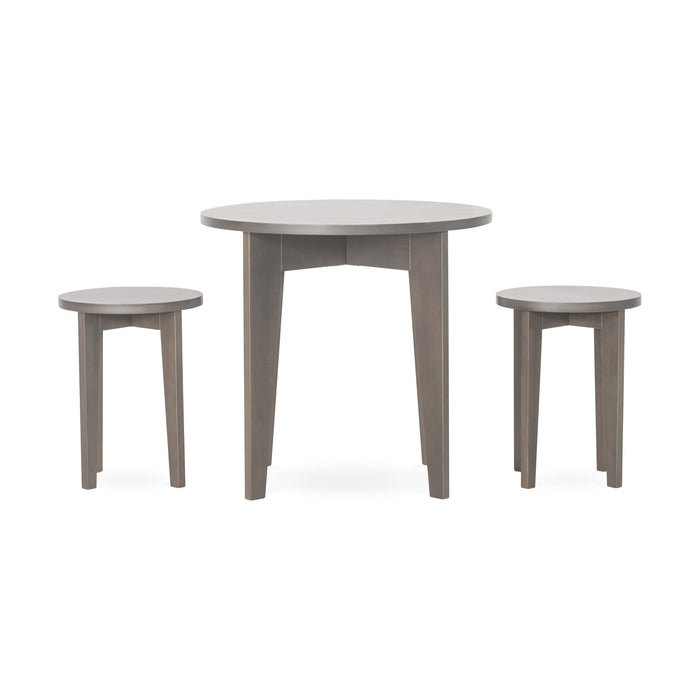 The Child Craft Geo Table and Stools Set in Dapper Gray features a round wooden table with three legs, paired with two matching round three-legged stools, all in a light grayish-brown finish against a plain white background.