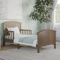 The Child Craft Hampton Toddler Bed in Dusty Heather is shown with a white pillow and bedding on a light gray rug in a softly decorated bedroom featuring star-patterned wallpaper, a potted tree, and curtained window.