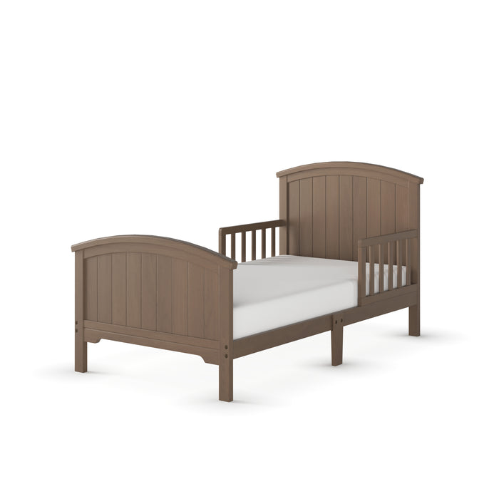 The Child Craft Hampton Toddler Bed in Dusty Heather features slatted sides, arched headboard and footboard, and comes with a simple mattress. Shown against a plain white background.