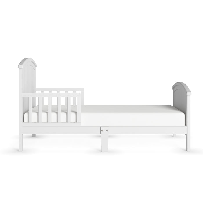 The Child Craft Hampton Toddler Bed in Matte White is a low-profile bed with a guard rail on one side, simple headboard and footboard, and includes a mattress. Shown against a plain white background.