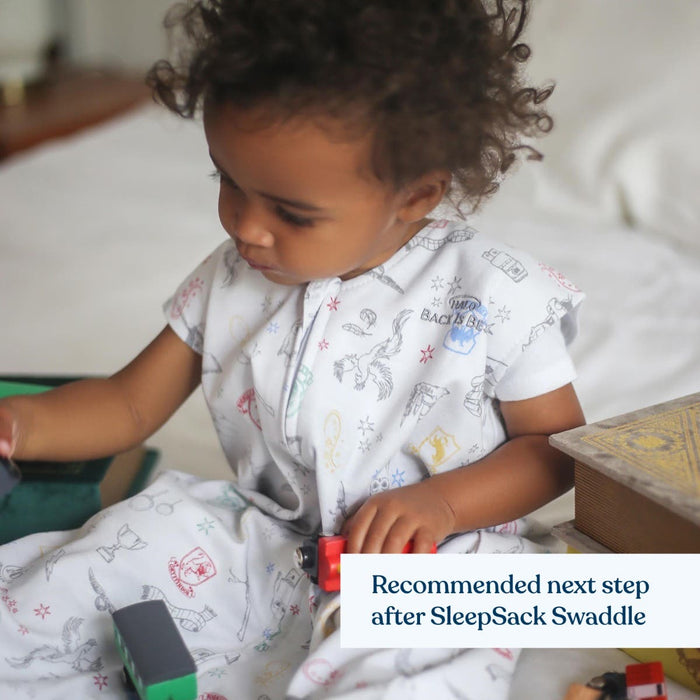 A toddler in a HALO Harry Potter™ Wearable Blanket 100% Cotton TOG 0.5 plays with a wooden train on a bed; the tag reads Back is Best. The text overlay suggests its the next step after using the SleepSack Swaddle for hip-healthy sleep.