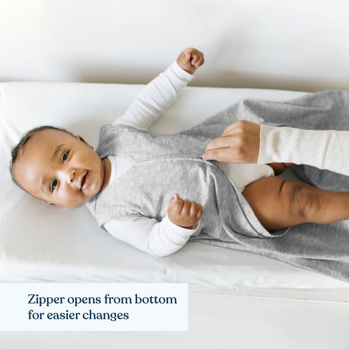 A happy baby lies on a changing table in a gray HALO Harry Potter™ Wearable Blanket 100% Cotton TOG 0.5, while an adult hand adjusts the bottom zipper. Caption: Zipper opens from bottom for easier changes and is hip healthy.
