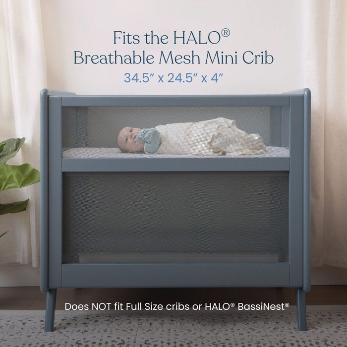 A baby rests on HALO Mini Crib Sheet 100% Cotton 2-Pack in a blue HALO Breathable Mesh Mini Crib (34.5 x 24.5 x 4). Text: Fits only the HALO Mini Crib, not for full-size cribs or HALO BassiNest.