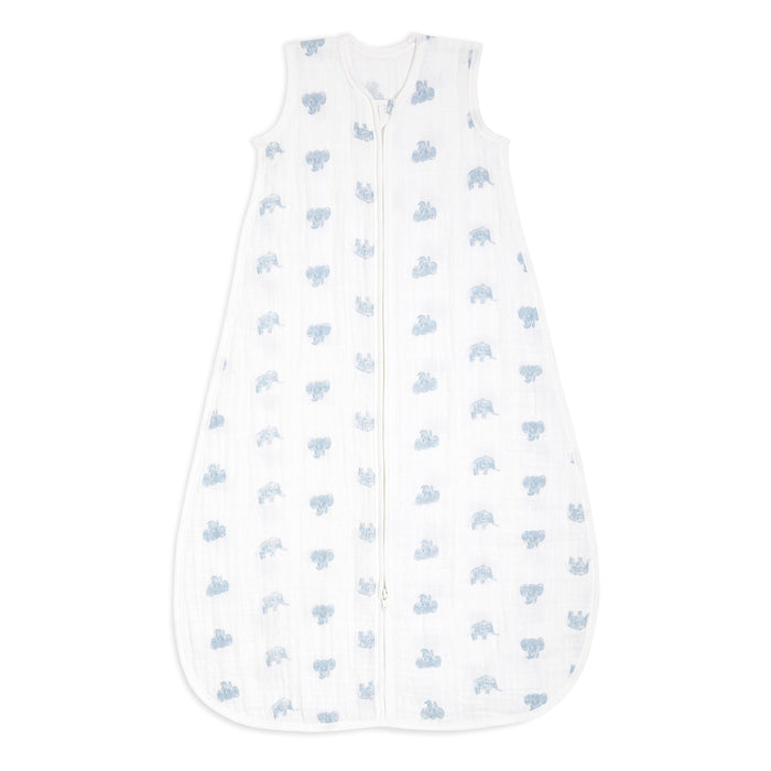 The aden + anais organic cotton light sleep sack TOG 1.0 is a sleeveless, white baby sleeping bag crafted from 100% organic cotton muslin with a front zipper. Featuring light blue elephants, it offers a cozy and breathable design for infants and is GOTS certified for safe and comfortable sleep.