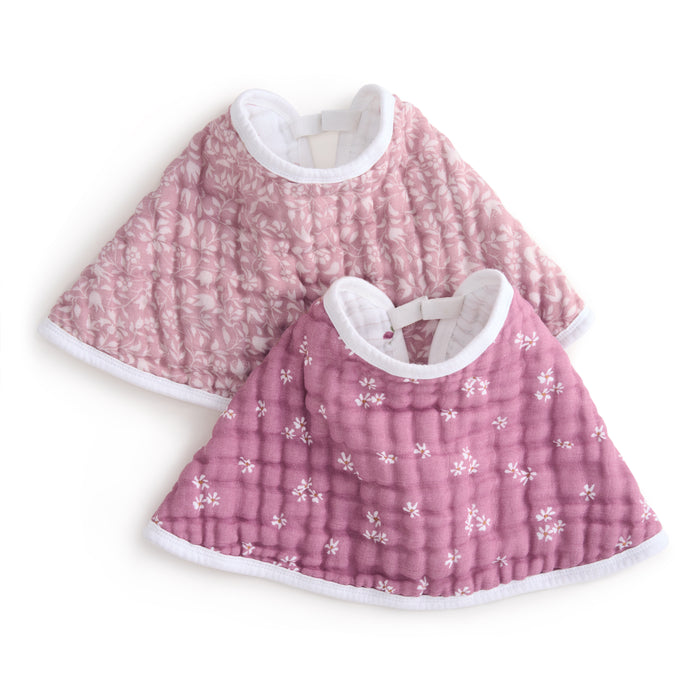 Two aden + anais organic cotton muslin burpy bibs feature a light pink version with a subtle flower pattern and a darker pink one with scattered small flowers, both crafted from GOTS certified organic cotton and displayed overlapping on a crisp white background for style and sustainability.