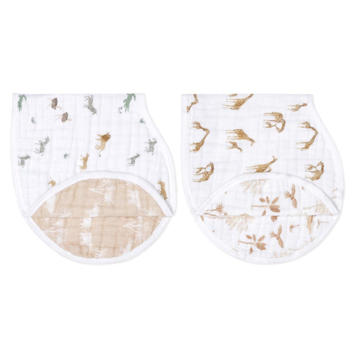 The aden + anais organic cotton muslin burpy bibs 2 pack includes two GOTS certified burp cloths. Both white with animal prints: green/brown dinosaurs on one, and brown giraffes/zebras on the other. They feature curved beige undersides with a white leaf design.