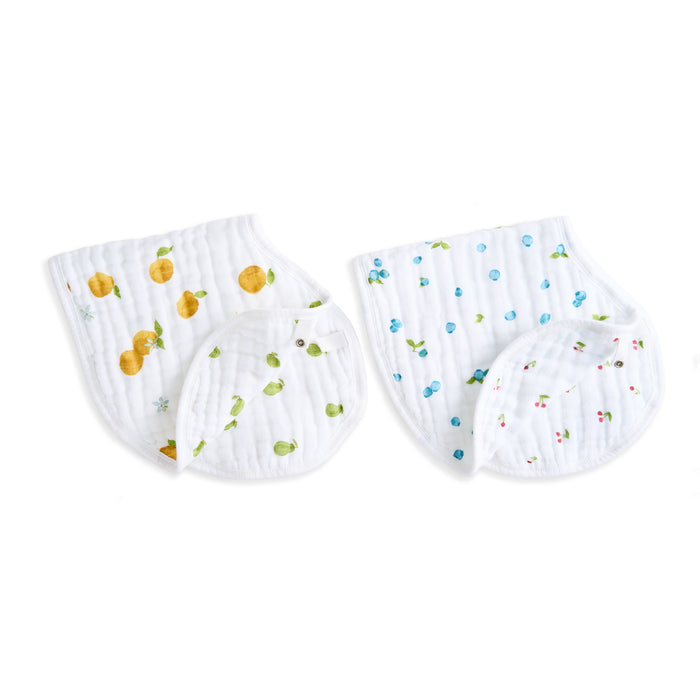 Aden + anais organic cotton muslin burpy bibs 2 pack includes two white quilted bibs with colorful fruit patterns; one dazzles with yellow lemons and the other features blue and red berries with green leaves. Both have scalloped edges, made from GOTS certified organic cotton, suitable as burp cloths.