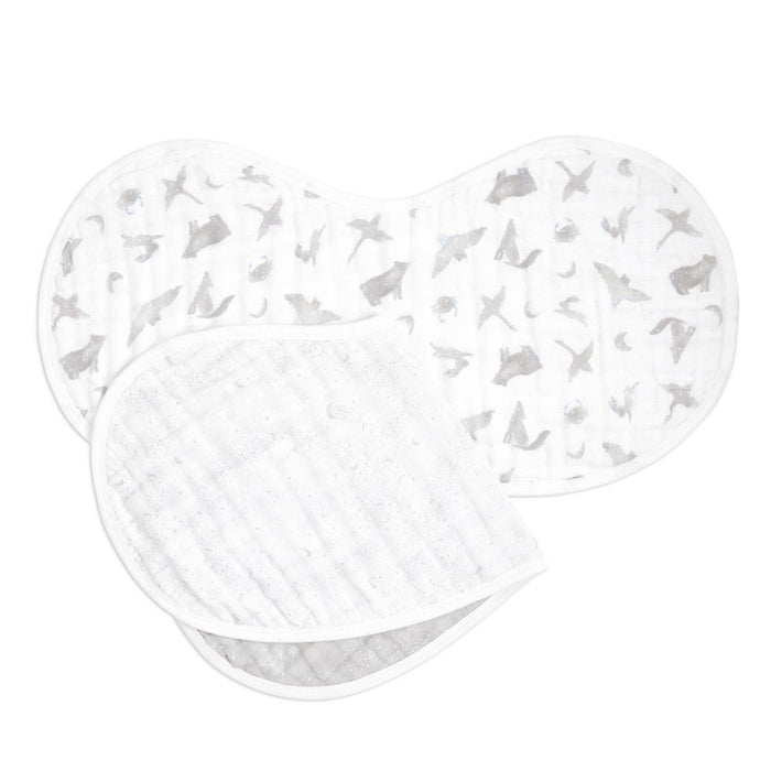 Displayed are two aden + anais organic cotton muslin burpy bibs: one with gray and silver stars, the other plain white. Both GOTS certified, they feature rounded edges and are layered together.