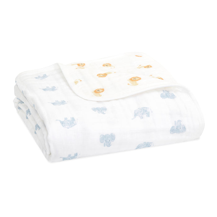 A folded aden + anais organic cotton dream blanket, GOTS certified, showcases charming blue elephant prints on soft muslin. The second corner playfully features delightful orange lion prints.