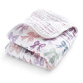 The aden + anais organic cotton muslin dream blanket is shown folded, featuring a white background with pastel bows in pink, purple, and green—perfect for crib bedding.