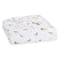 The aden + anais organic cotton dream blanket, crafted from GOTS certified white cotton muslin, showcases a charming pattern of giraffes, zebras, lions, and crocodiles in soft brown and gray tones.