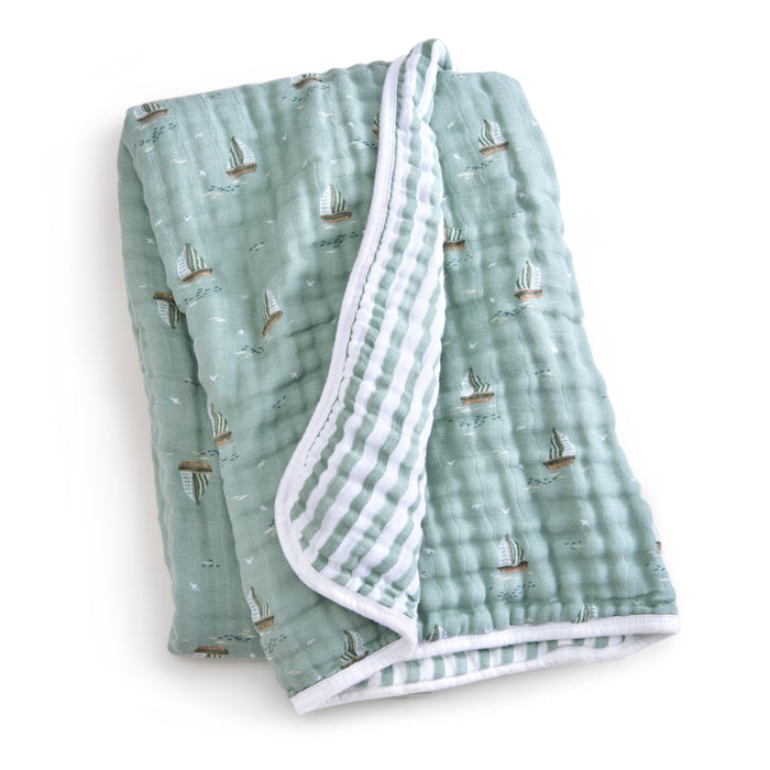 The aden + anais organic cotton muslin dream blanket is a soft, folded green baby blanket with a sailboat pattern made from GOTS certified organic materials. Its plush inner side features a striped design in white and gray tones for your little ones comfort.