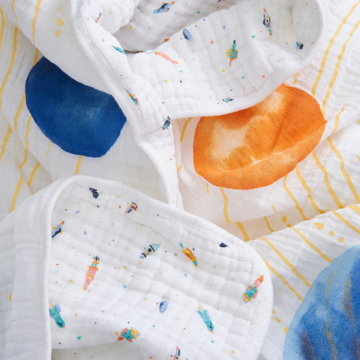 A close-up of the aden + anais organic cotton muslin dream blanket shows colorful planets, spaceships, bold orange and blue circles, and yellow orbits—ideal as crib bedding for babies.