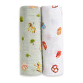 The aden + anais organic cotton muslin swaddle blanket 2 pack includes two blankets: one with green carousel horses and trees, and one white with assorted snacks like pretzels and pizza.