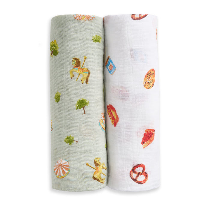 The aden + anais organic cotton muslin swaddle blanket 2 pack includes two blankets: one with green carousel horses and trees, and one white with assorted snacks like pretzels and pizza.