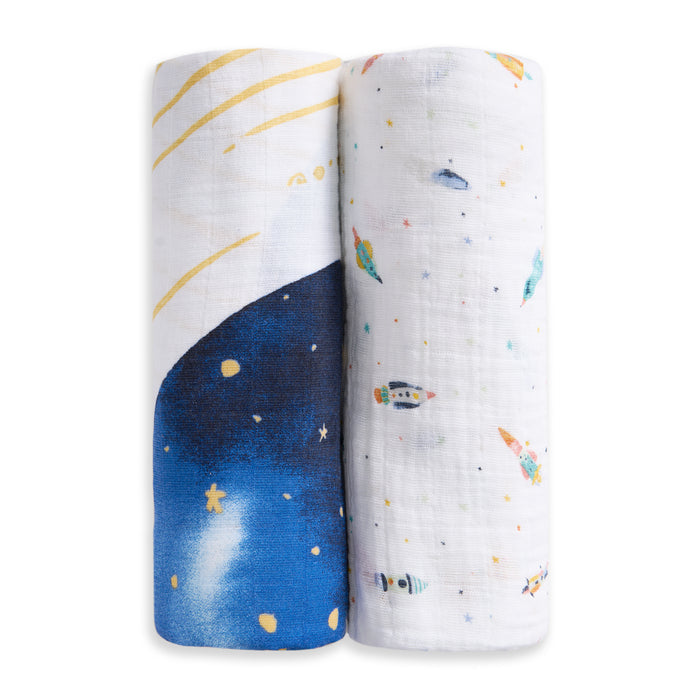 The aden + anais organic cotton muslin swaddle blanket 2 pack includes one blue night sky with yellow stars and one white blanket with colorful rockets, planets, and stars—ideal as a cozy baby muslin blanket set.