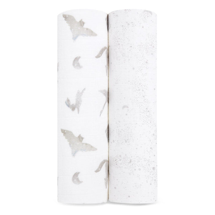 Two rolls of white fabric with subtle designs: gray bats and crescent moons on the left, and a dotted star pattern on the right. These soft, textured fabrics are ideal for creating aden + anaiss organic cotton muslin swaddle blanket 2 pack, which is GOTS certified.