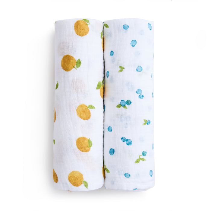 Aden + Anais organic cotton muslin swaddle blanket 2 pack, GOTS certified, includes two rolled blankets. One has an orange fruit print with green leaves, and the other features blue fruit-like patterns with green leaves, set side by side on a plain white background.