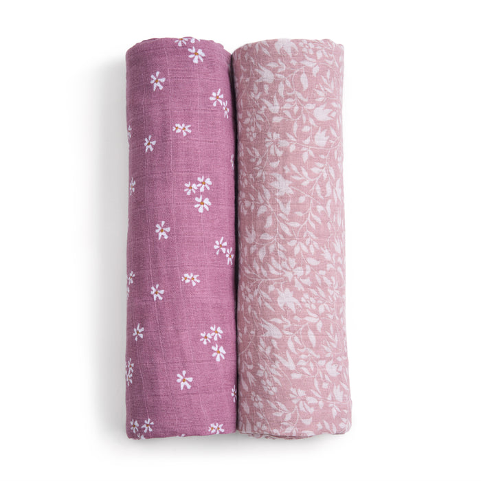 Two rolls of aden + anais organic cotton muslin swaddle blankets, each with soft GOTS-certified fabrics, stand side by side. The left roll displays small white floral prints, and the right shows a delicate white leaf pattern.