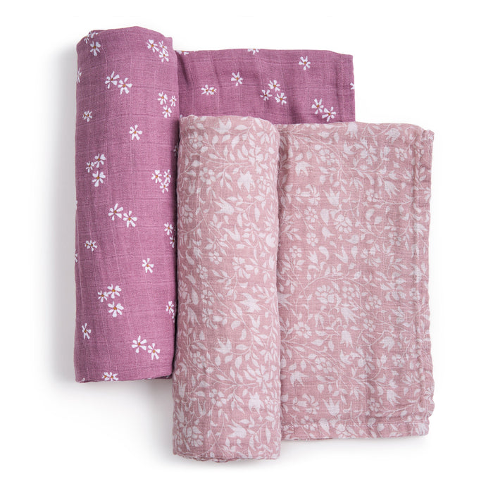 Displayed are three rolled organic cotton muslin swaddle blankets: two with purple backgrounds and white floral patterns, and one pink with a subtle floral design. These GOTS certified blankets from aden + anais offer charm and assurance.